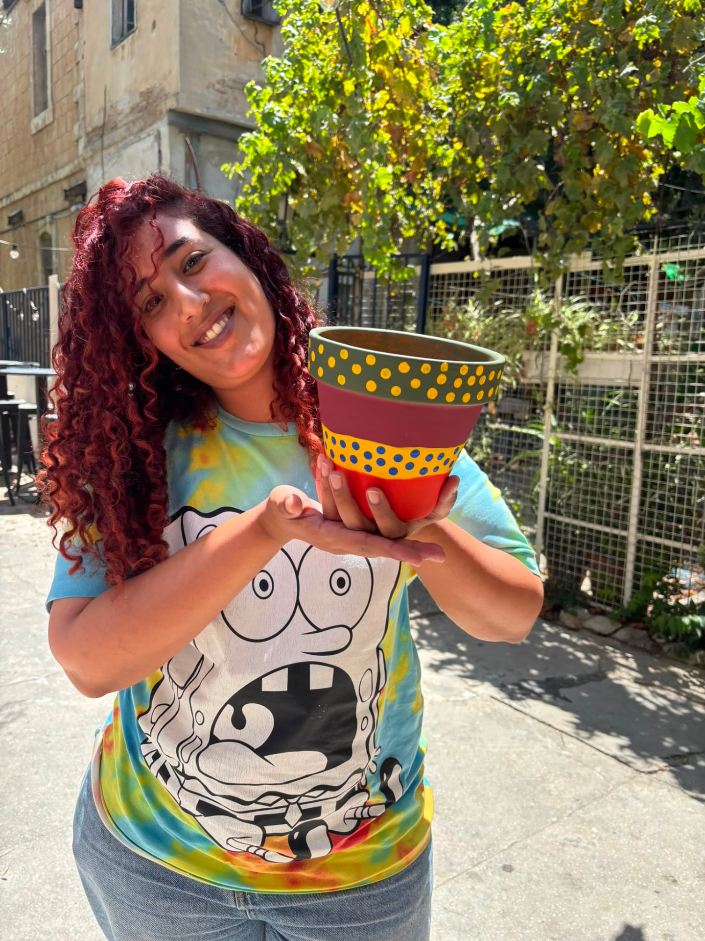 משתתפת מציגה עציץ טרקוטה צבעוני שציירה